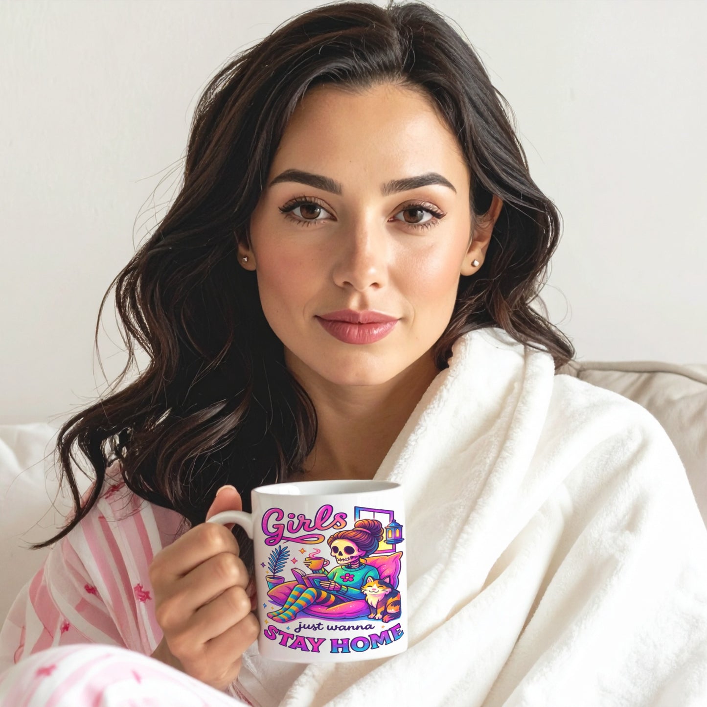 Woman sat on the sofa wrapped in a blanket holding a mug with colourful design and text saying Girls Just Wanna Stay Home