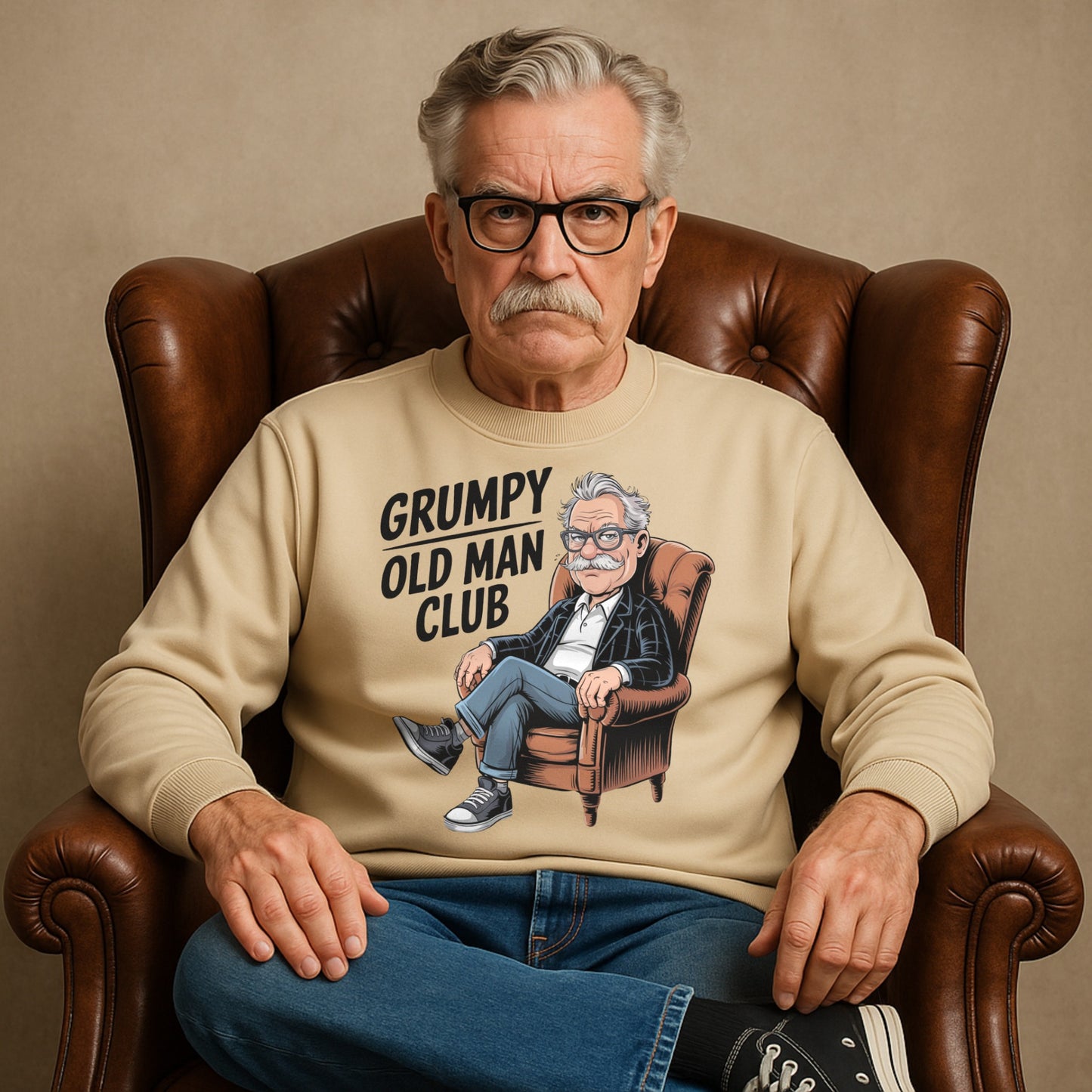 Man wearing a beige sweatshirt with 'Grumpy Old Man Club' graphic sitting in a brown leather chair.