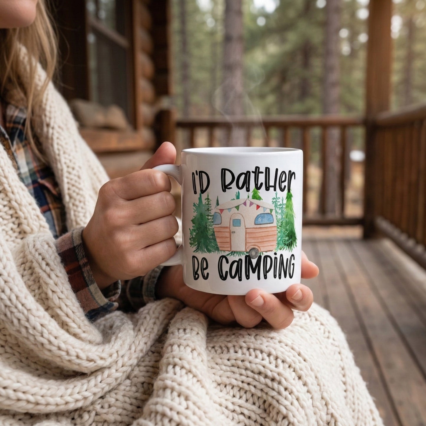 Woman relaxing on a cosy woodland cabin porch holding an I'd Rather Be Camping coffee mug featuring a vintage camper trailer, perfect for campers, caravan lovers, and outdoor adventures.