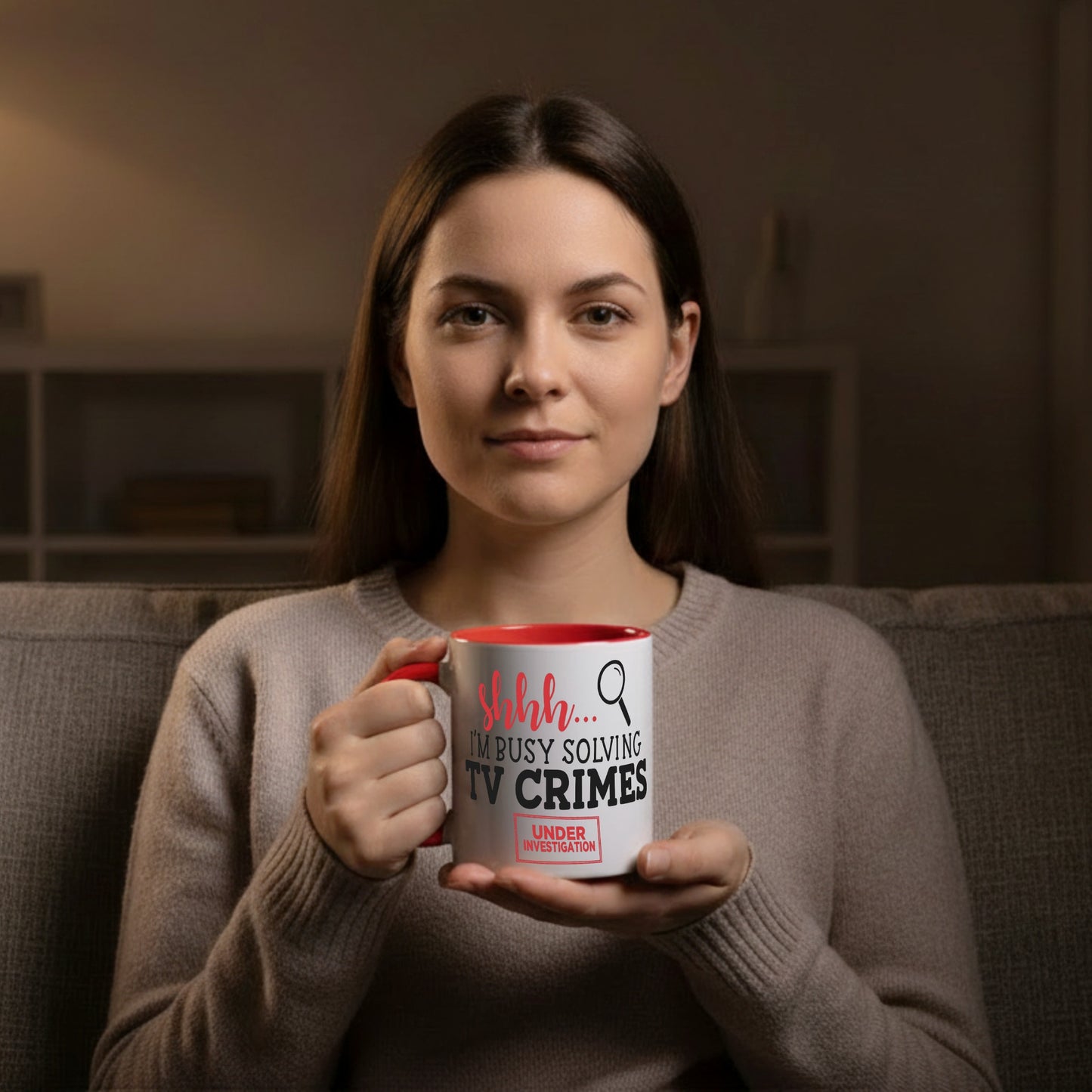 Woman relaxing on a sofa holding a Shhh I'm Busy Solving TV Crimes funny detective coffee mug with a red handle, perfect for true crime fans, detective TV show lovers, and mystery enthusiasts.