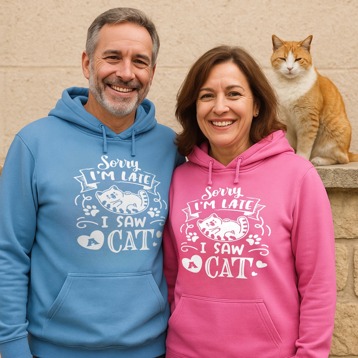 Two people wearing matching blue and pink hoodies with a cat in the background.