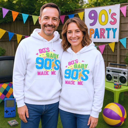 Two people wearing '80s Baby 90s Made Me' hoodies at a 90s party with decorations and a sign in the background.