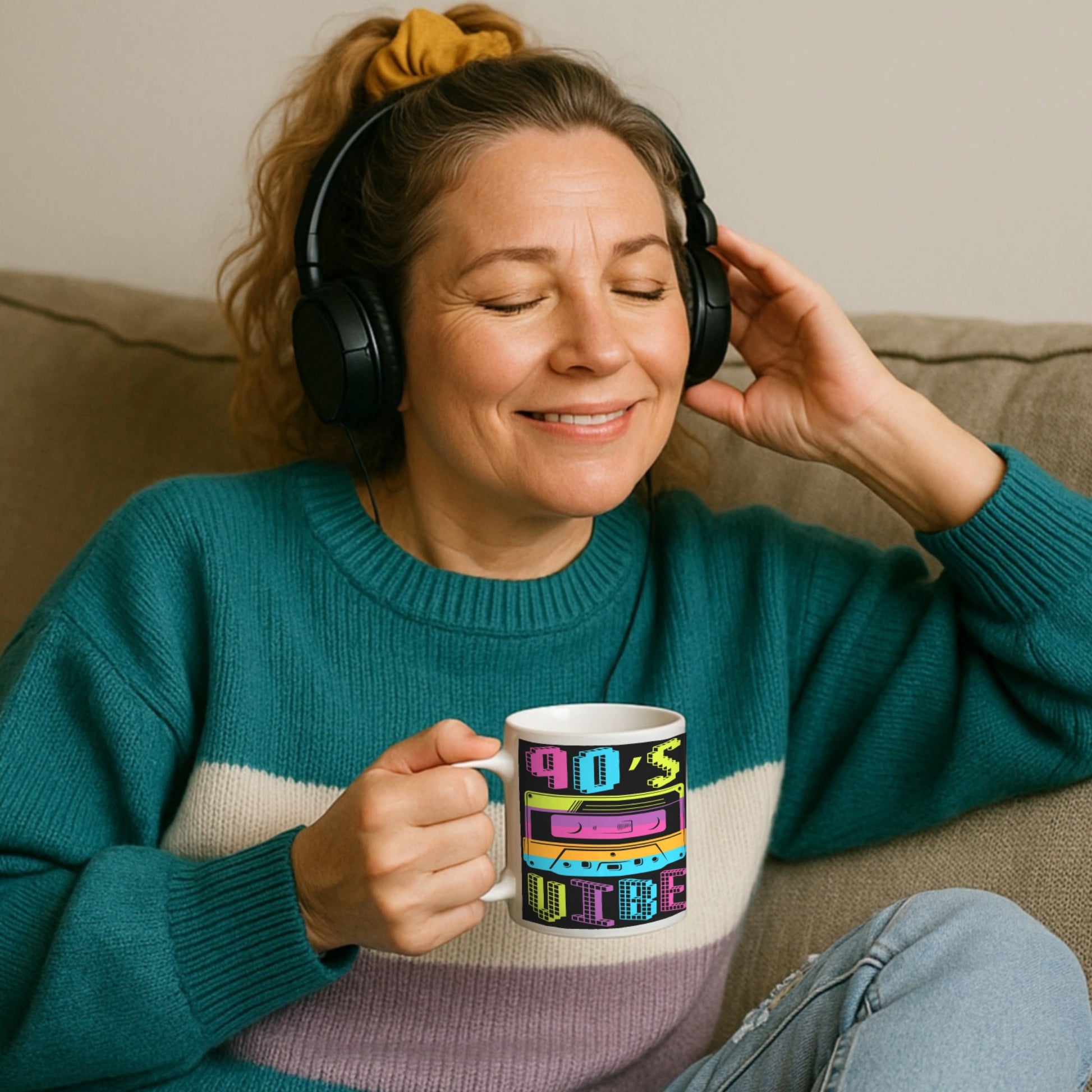 Woman wearing headphones and holding a 90s vibe mug with colourful text, sitting on a couch.