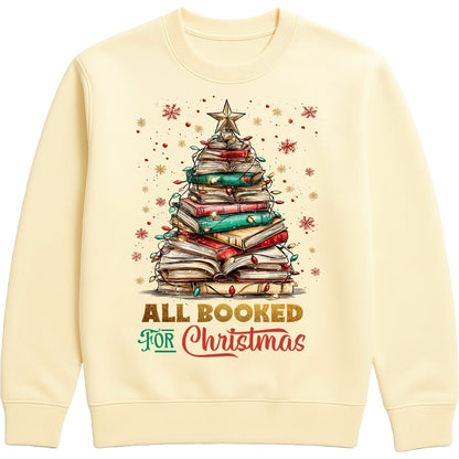 Vanilla milkshake colour “All Booked for Christmas” sweatshirt featuring a whimsical book-stack Christmas tree with lights and a star, styled in a cozy holiday aesthetic.