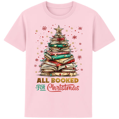 Pink festive bookish Christmas t-shirt featuring a Christmas tree made of stacked books, surrounded by twinkle lights and warm winter vibes.