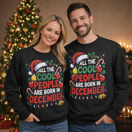 Couple wearing matching All The Cool People Are Born In December sweatshirts with festive Christmas typography, Santa hats, holly, candy canes, and Christmas lights, posing in front of a decorated Christmas tree, perfect Christmas birthday sweatshirts and December birthday gifts.
