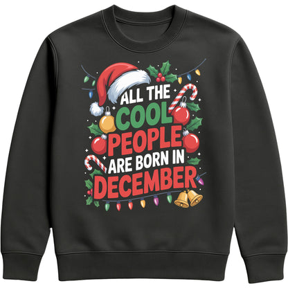 All The Cool People Are Born In December sweatshirt featuring festive Christmas typography with a Santa hat, candy canes, holly, baubles, bells, and colourful Christmas lights on a black unisex sweatshirt, perfect funny Christmas birthday sweatshirt and December birthday gift.