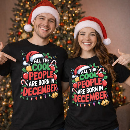 Couple wearing matching All The Cool People Are Born In December T-Shirts with festive Christmas design, Santa hats, and Christmas tree backdrop, perfect funny December birthday shirts and Christmas birthday gifts.