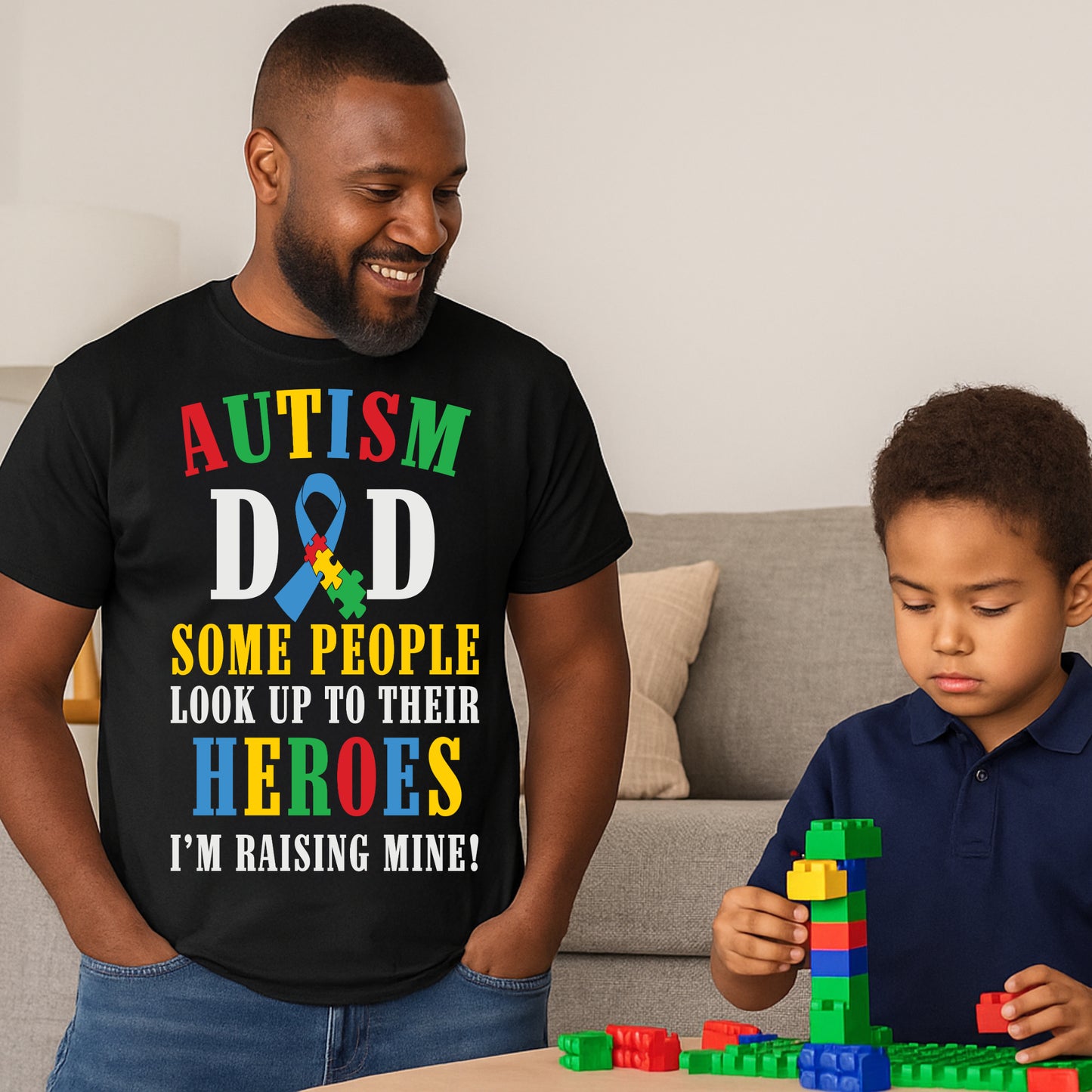 Man wearing a black t-shirt with autism awareness message, standing next to a child playing with building blocks. the text on the t-shirt reads: AUTISM DAD SOME PEOPLE LOOK UP TO THEIR HEROES I'M RAISING MINE  The design celebrates fatherhood and pride in raising a child with autism.
