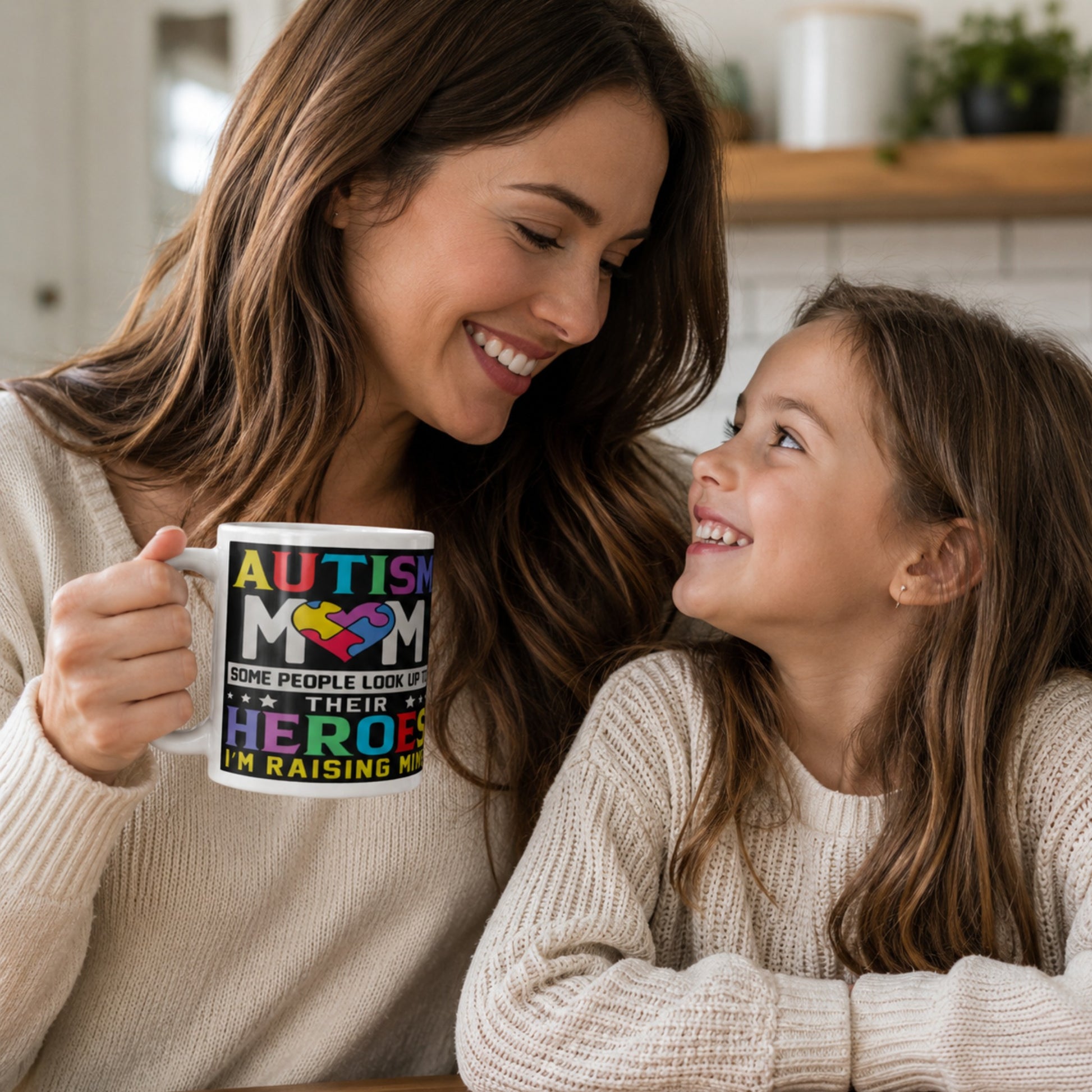 Autism mum sharing a special moment with her daughter while holding an Autism Mom mug featuring a colourful puzzle heart design and “Some People Look Up To Their Heroes I'm Raising Mine” message.