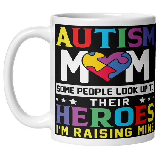 White Autism Mom mug featuring a colourful puzzle heart design and the quote “Some People Look Up To Their Heroes I'm Raising Mine” promoting autism awareness, acceptance, and support.