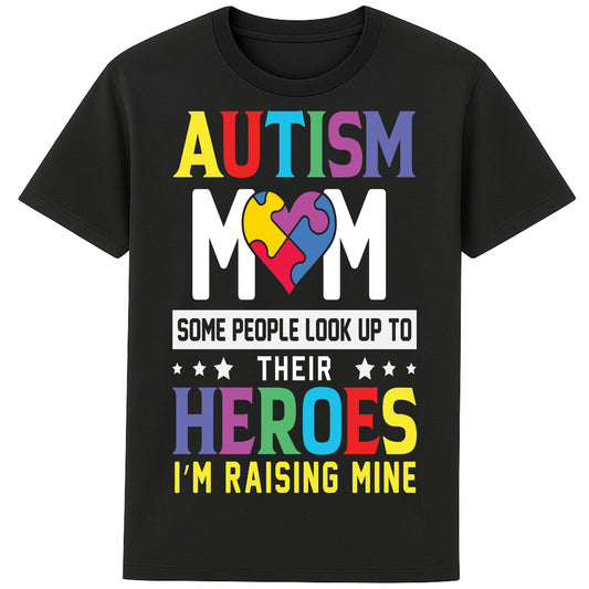 A black t-shirt with bold, colorful text reading: "AUTISM MOM" at the top, each letter in a different color. Below it, a heart-shaped puzzle piece design in multiple vibrant colors. Underneath, the text says: "SOME PEOPLE LOOK UP TO THEIR HEROES I'M RAISING MINE," with "HEROES" emphasized in large, colorful letters. The design celebrates motherhood and pride in raising a child with autism.
