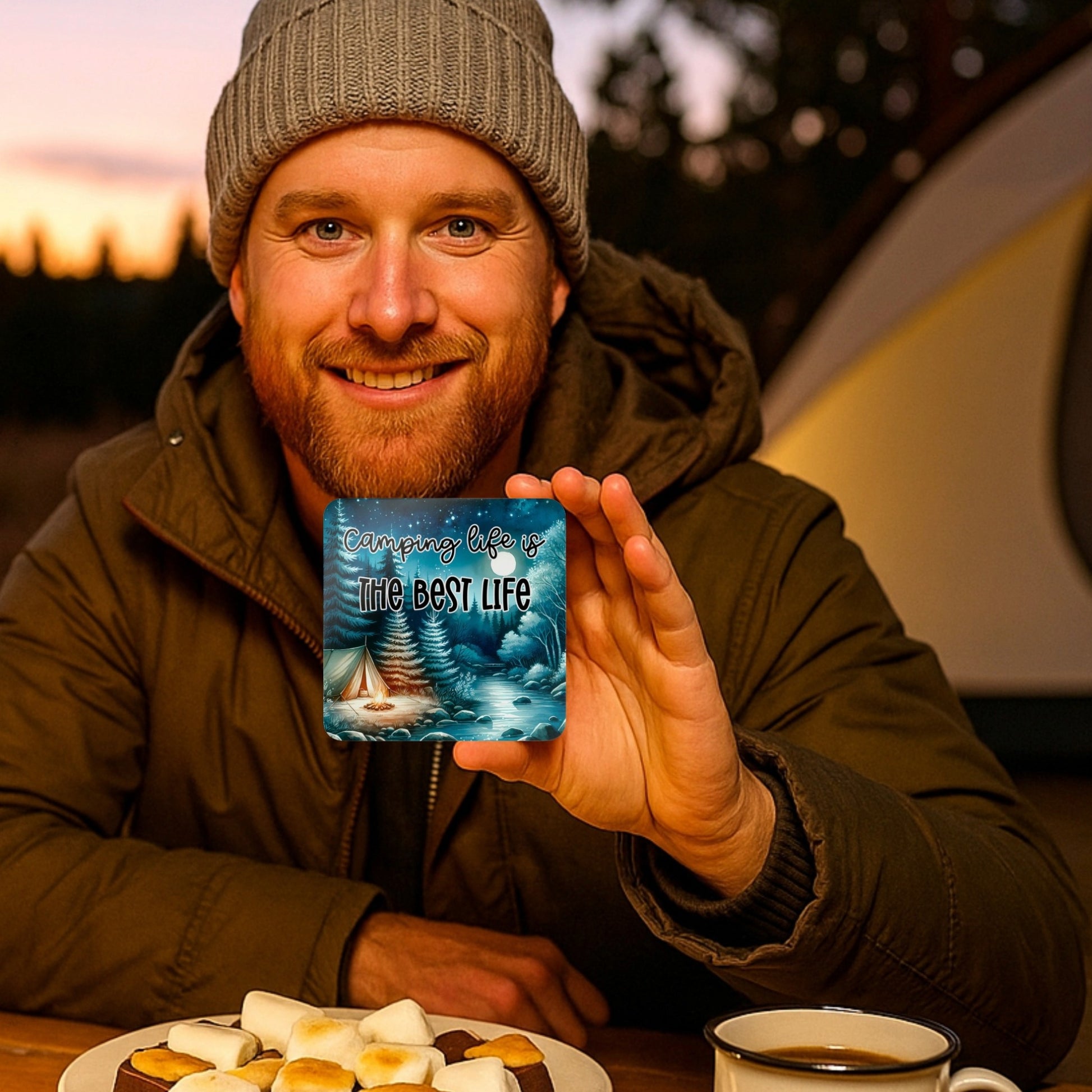 Man holding a card with 'Camping is the best life' text, surrounded by camping gear.