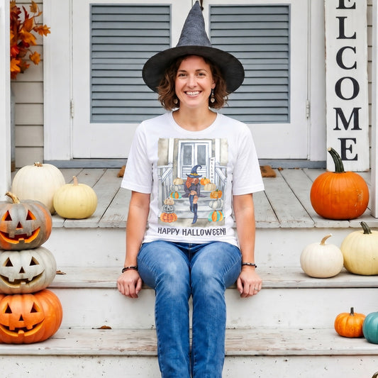 Smiling woman wearing a Chic Witch Halloween Shirt while sitting on a pumpkin-decorated front porch. Cute witch graphic tee featuring autumn pumpkins, Halloween artwork, and cosy fall season style.