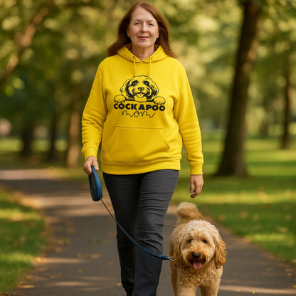 Woman walking her Cockapoo in a park while wearing a yellow Cockapoo Mom hoodie featuring a cute Cockapoo dog graphic, perfect for dog mums and Cockapoo lovers.