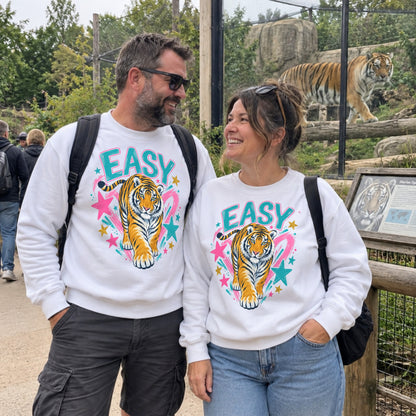 Man and woman wearing matching Easy Tiger graphic sweatshirts beside a tiger enclosure at a wildlife park.