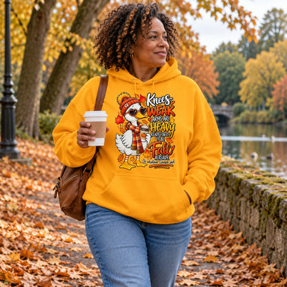 Woman wearing an gold colour funny fall goose hoodie with autumn leaves and coffee artwork while walking through a leafy park.