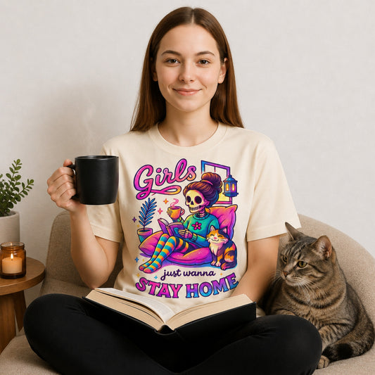 Woman wearing the Girls Just Wanna Stay Home T-Shirt with a steaming coffee, open book, and grey tabby cat, featuring a colourful skeleton graphic, a funny homebody shirt for book lovers, introverts, and cat lovers.
