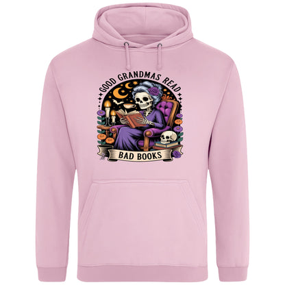Pink Good Grandmas Read Bad Books Hoodie featuring a spooky cute skeleton grandma reading in a cosy armchair with candles and flowers, funny grandma hoodie for book lovers and gothic readers.