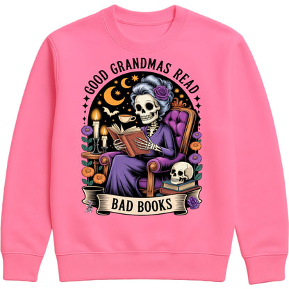 Candyfloss pink Good Grandmas Read Bad Books Sweatshirt featuring a spooky cute skeleton grandma reading in a cosy armchair with candles, flowers, and moon details, funny grandma sweatshirt for book lovers and gothic book lovers.