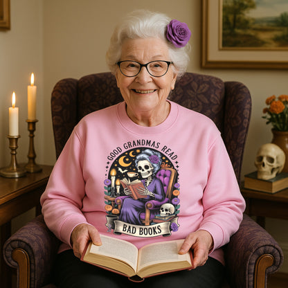 Smiling grandma wearing the Good Grandmas Read Bad Books Sweatshirt while reading a book in a cosy armchair with candles, flowers, and gothic décor, funny grandma sweatshirt for book lovers and gothic book lovers.