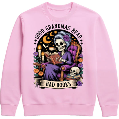 Pink Good Grandmas Read Bad Books Sweatshirt featuring a spooky cute skeleton grandma reading in a cosy armchair with candles, flowers, and moon details, funny grandma sweatshirt for book lovers and gothic book lovers.