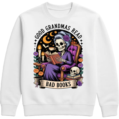 White Good Grandmas Read Bad Books Sweatshirt featuring a spooky cute skeleton grandma reading in a cosy armchair with candles, flowers, and moon details, funny grandma sweatshirt for book lovers and gothic book lovers.