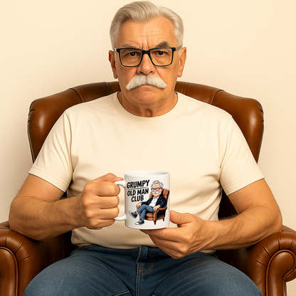 Older man sitting in a brown leather armchair holding a Grumpy Old Man Club coffee mug featuring a cartoon grumpy old man design. Funny old man mug, retirement gift for men, funny dad mug, and grandad gift.