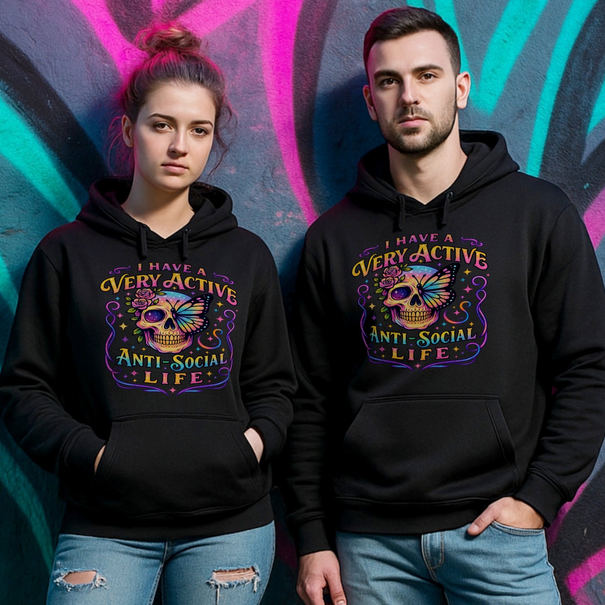 Two people wearing a black hoodie with “I Have a Very Active Anti-Social Life” print with a colourful skull, rose, and butterfly graphic — bold streetwear for cosy anti-social vibes.