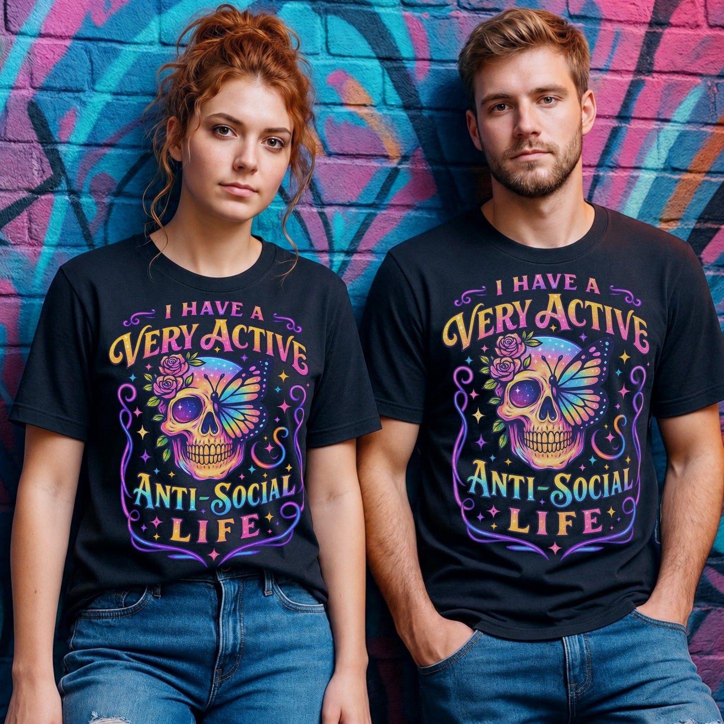 Male and female models wearing the I Have A Very Active Anti Social Life T-shirt featuring a colourful neon sugar skull, butterfly, and floral graphic on black unisex graphic tees against a vibrant graffiti wall.