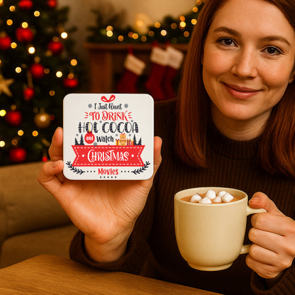 A woman holding a festive coaster with the phrase "I Just Want to Drink Hot Cocoa and Watch Christmas Movies" featuring holiday graphics like a teddy bear and snowflakes.