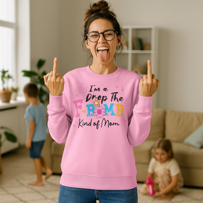 Mom wearing a baby pink "I'm A Drop The F-Bomb Kind Of Mom" funny motherhood sweatshirt with colourful retro lettering while standing at home with children in the background.