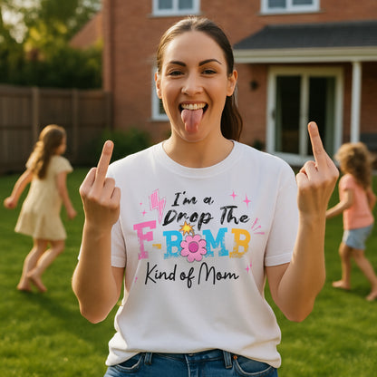 "A woman wearing a white t-shirt with colorful text reading ‘I’m a Drop the F-Bomb Kind of Mom’ with sparkles, lightning bolts, and flower graphic."