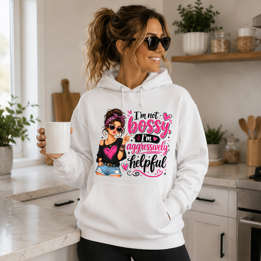 Woman wearing a white "I'm Not Bossy, I'm Aggressively Helpful" graphic hoodie in a bright modern kitchen, holding a coffee mug in a relaxed lifestyle mockup.
