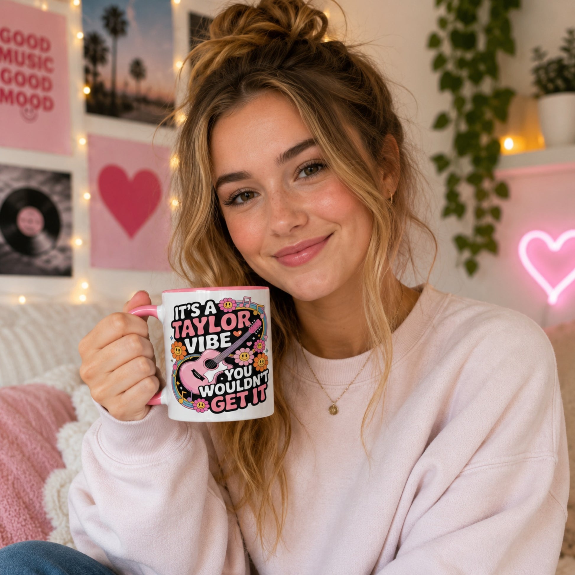 Young woman holding the It's A Taylor Vibe You Wouldn't Get It retro music coffee mug with a pink handle in a cosy music-inspired bedroom featuring pastel décor, vinyl records, fairy lights, and colourful wall art.