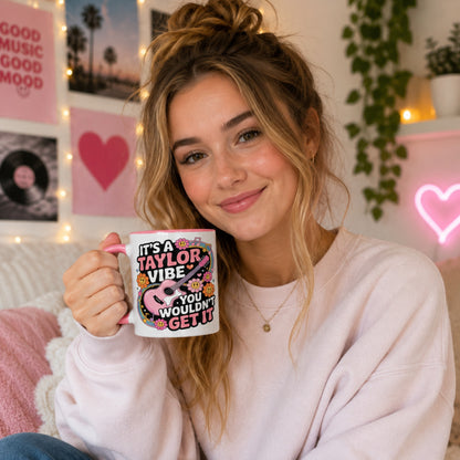 Young woman holding the It's A Taylor Vibe You Wouldn't Get It retro music coffee mug with a pink handle in a cosy music-inspired bedroom featuring pastel décor, vinyl records, fairy lights, and colourful wall art.