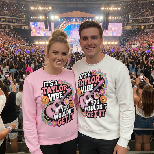 Lifestyle mockup of two fans wearing the It's A Taylor Vibe You Wouldn't Get It retro music fan sweatshirts at a vibrant live concert with colourful stage lights, cheering crowd, and a fun music festival atmosphere.