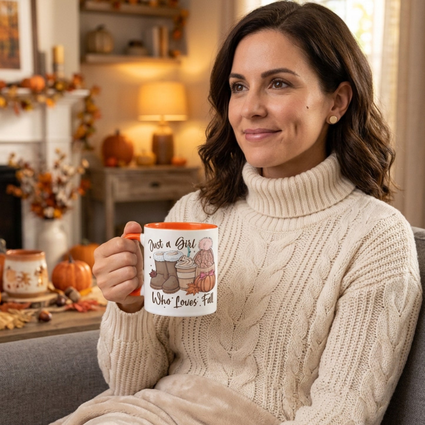 Woman relaxing at home holding the Just A Girl Who Loves Fall colour mug featuring autumn boots, a pumpkin spice latte, knitted beanie, colourful fall leaves and pumpkin artwork in a cosy autumn living room