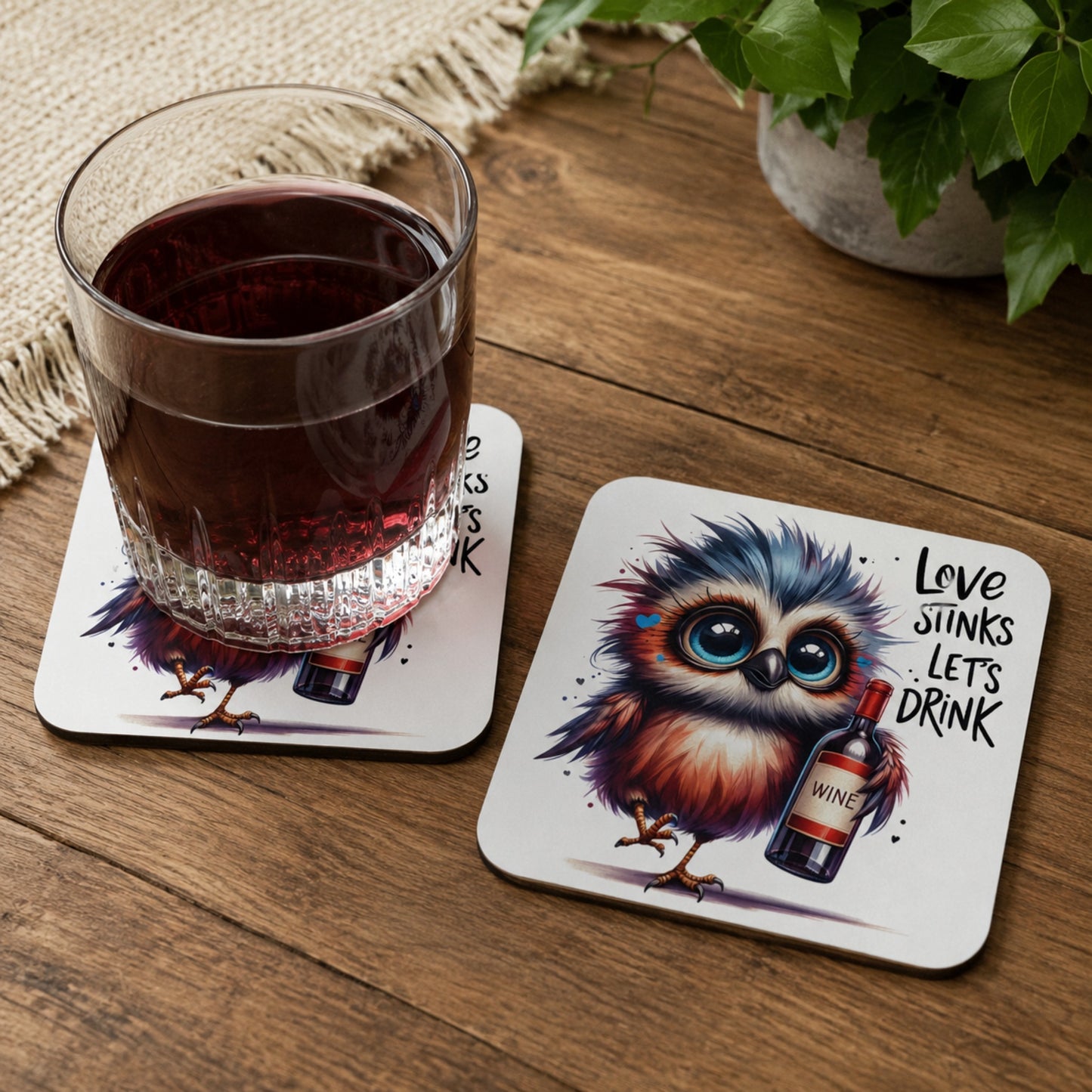 Lifestyle mockup of the Love Stinks Let's Drink owl wine coaster with a glass of red wine resting on one coaster and a second matching coaster displayed alongside on a rustic wooden table.
