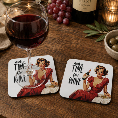 Lifestyle mockup of the Make Time For Wine retro coaster with a glass of red wine resting on one coaster and a second matching coaster displayed beside it on a rustic wooden table with grapes, a wine bottle and cosy candlelight.