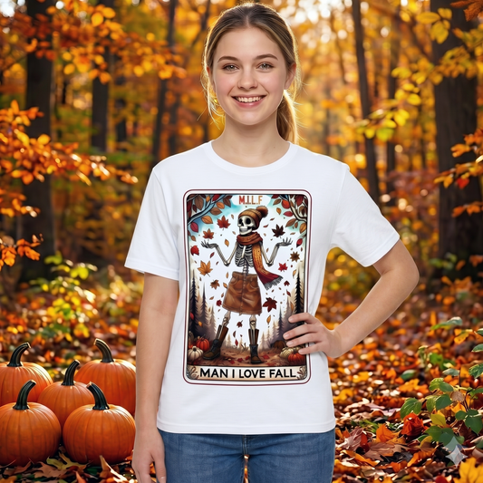 Young woman wearing a white M.I.L.F. (Man I Love Fall) t-shirt featuring a stylish skeleton surrounded by autumn leaves and pumpkins, standing in a colourful fall woodland setting. Funny autumn graphic tee for pumpkin spice lovers, Halloween fans, and fall enthusiasts