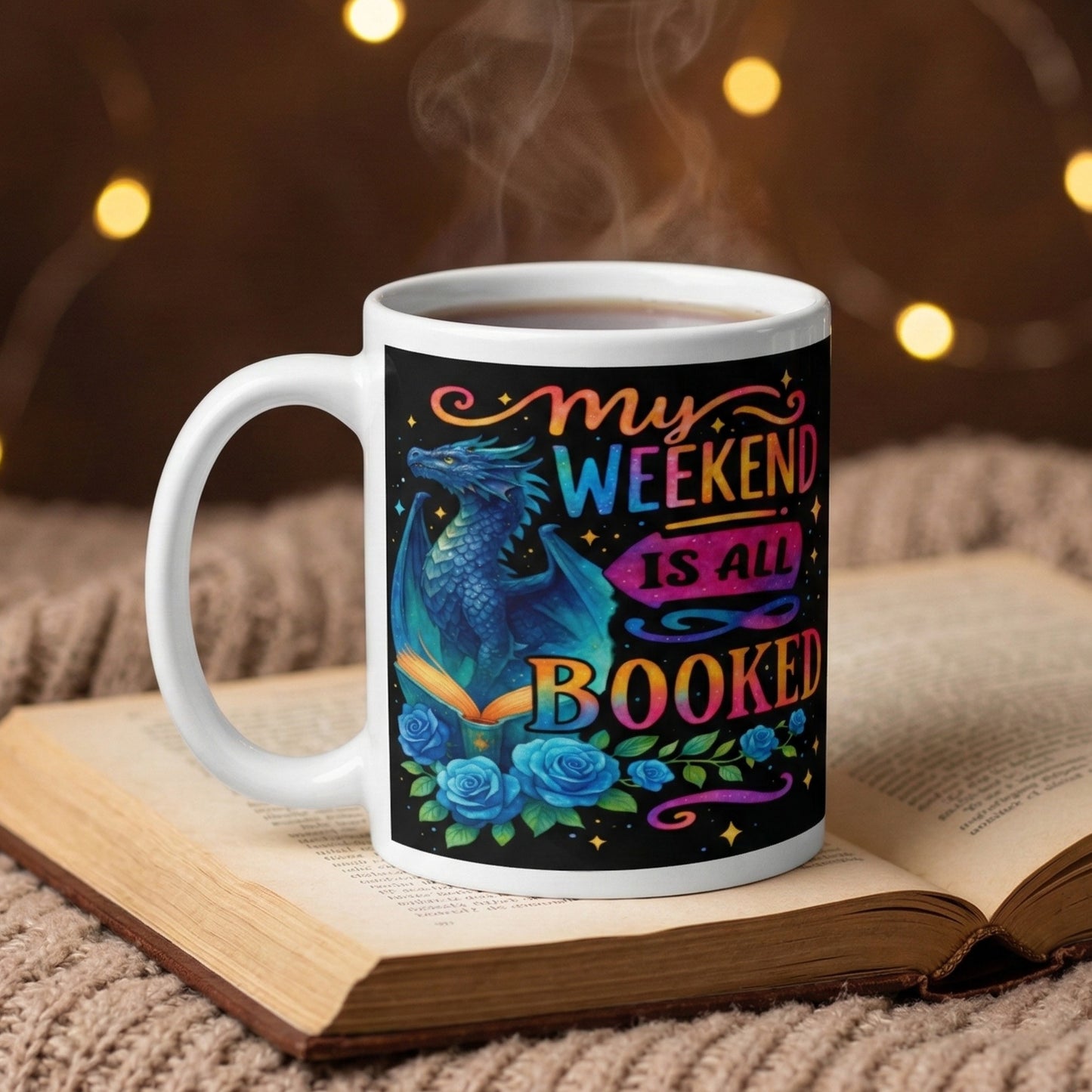 My Weekend Is All Booked book lover coffee mug featuring a blue fantasy dragon and enchanted book design resting on an open book with hot coffee in a cosy reading nook.