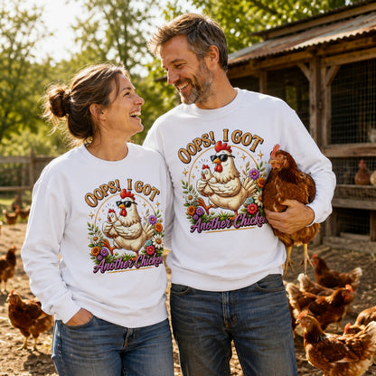 Couple wearing Oops! I Got Another Chicken Sweatshirts while smiling in a chicken coop, surrounded by backyard hens, with one holding a chicken.