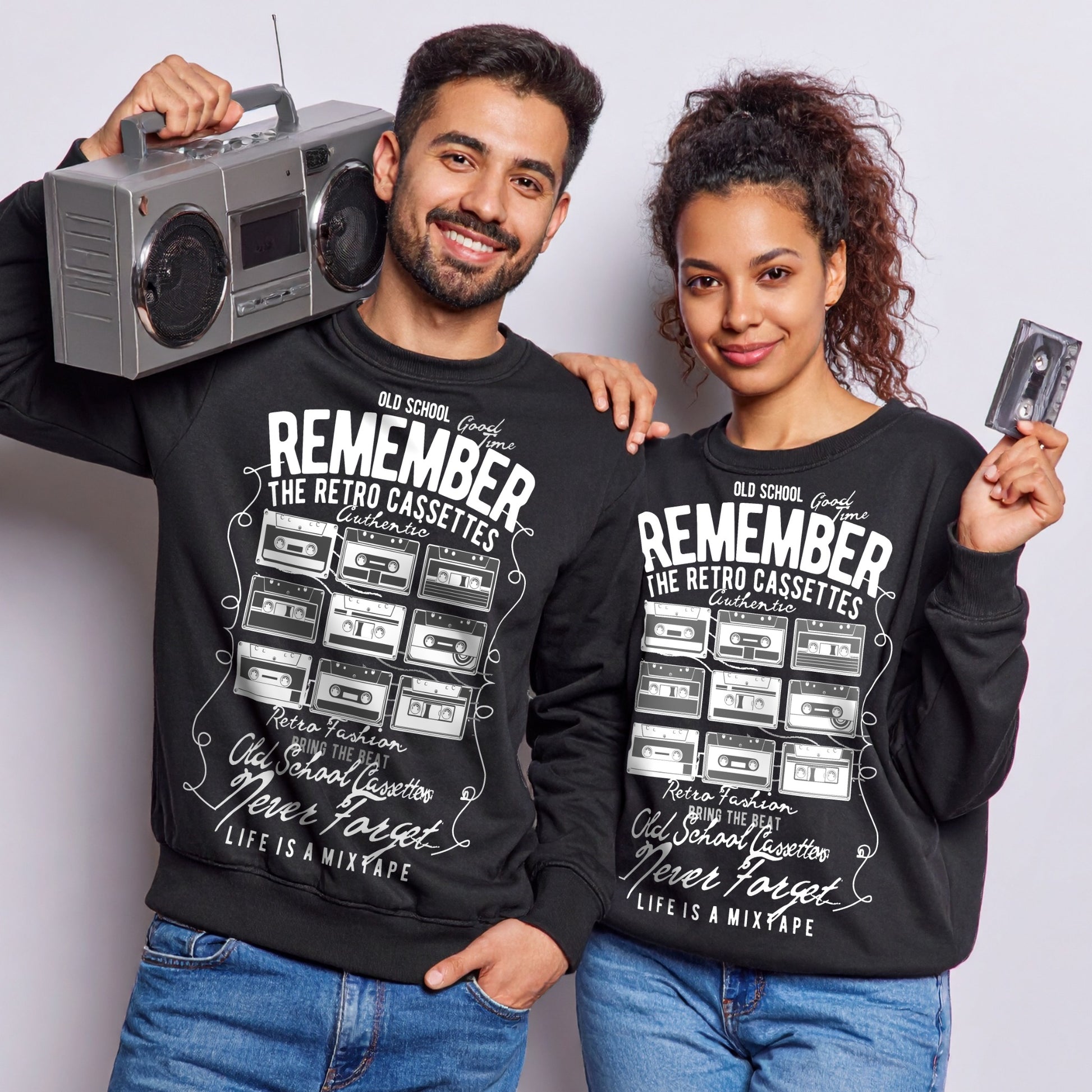 Two people wearing matching black sweatshirts with retro cassette design, holding a boombox and a cassette.