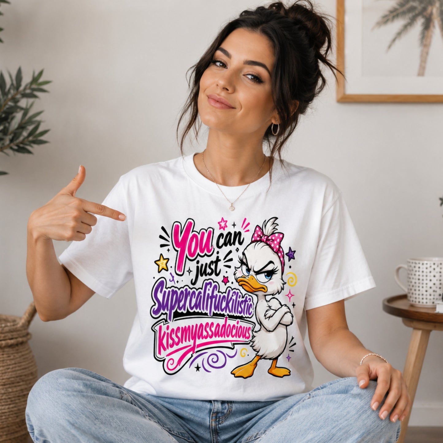 Female model wearing a white sarcastic grumpy duck T-shirt with the funny quote "You Can Just Supercalifuckilistic Kissmyassadocious", styled with relaxed fit jeans and white trainers in a bright lifestyle setting.