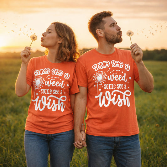 Couple wearing Some See A Weed Some See A Wish dandelion t-shirts while blowing dandelion seeds in a countryside field at sunset. Inspirational nature lover graphic tees with a positive quote.
