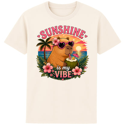 Naturel colour Sunshine Is My Vibe Capybara T-Shirt featuring a cute capybara wearing heart-shaped sunglasses, holding a coconut drink with tropical flowers, palm trees and a colourful summer beach sunset graphic.