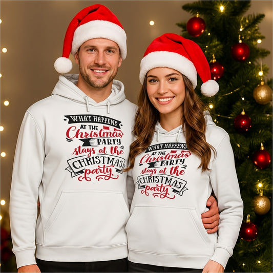 Couple wearing matching white What Happens At The Christmas Party hoodies with Santa hats beside a decorated Christmas tree. Funny Christmas hoodie for office Christmas parties, festive celebrations, holiday gatherings, and Christmas gifts.